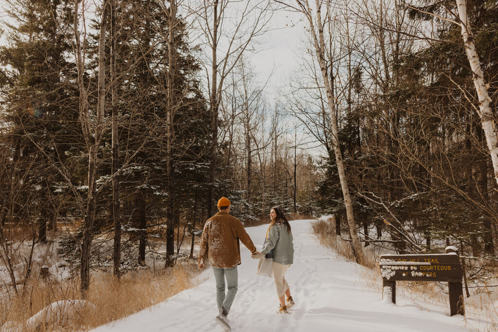 Engaged couple walks along trail during winter engagement shoot in North Shore, Minnesota