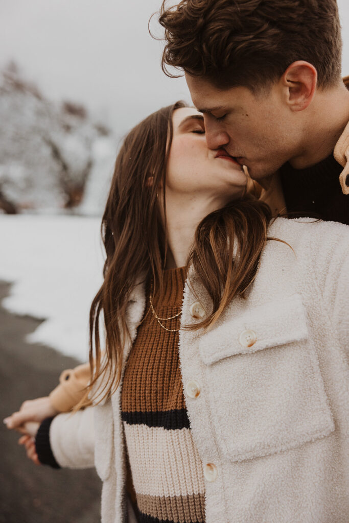 Man and woman kiss on Black Beach during winter destination engagement