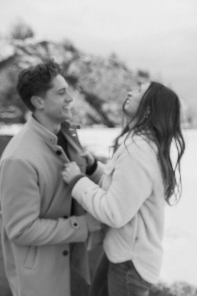 Woman grips collar of fiance's peacoat as they play in the snow