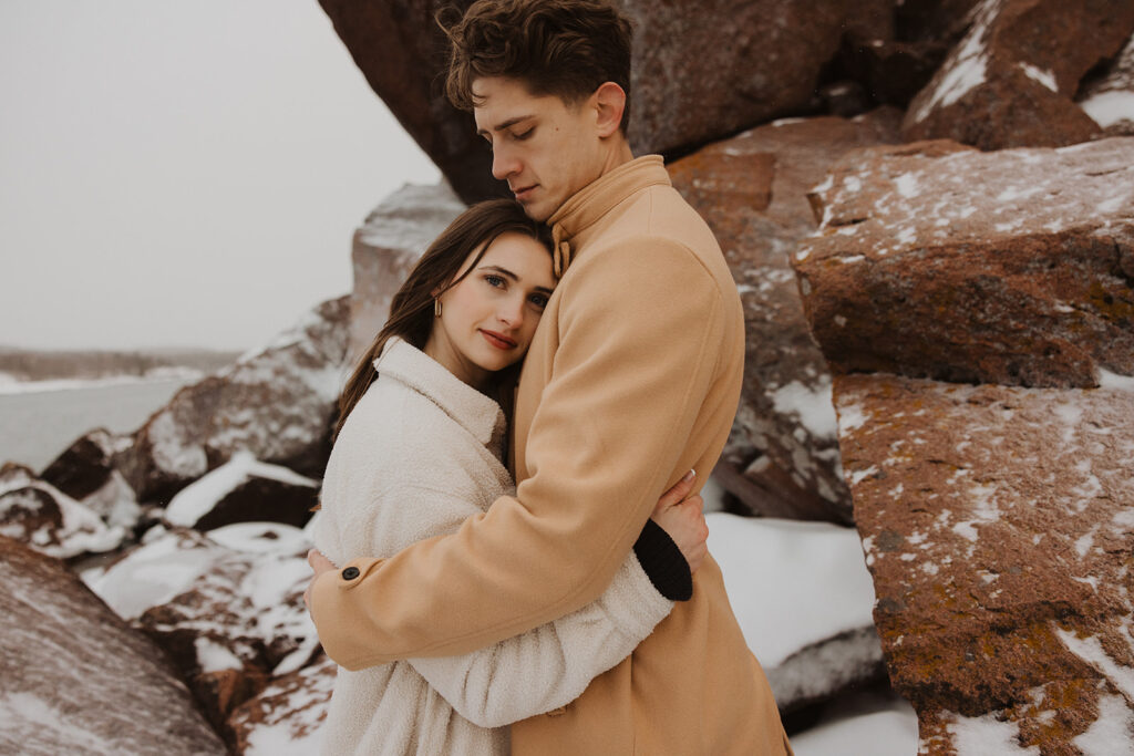 Woman lays her head on man's chest as he wraps her in warm embrace during winter destination engagement