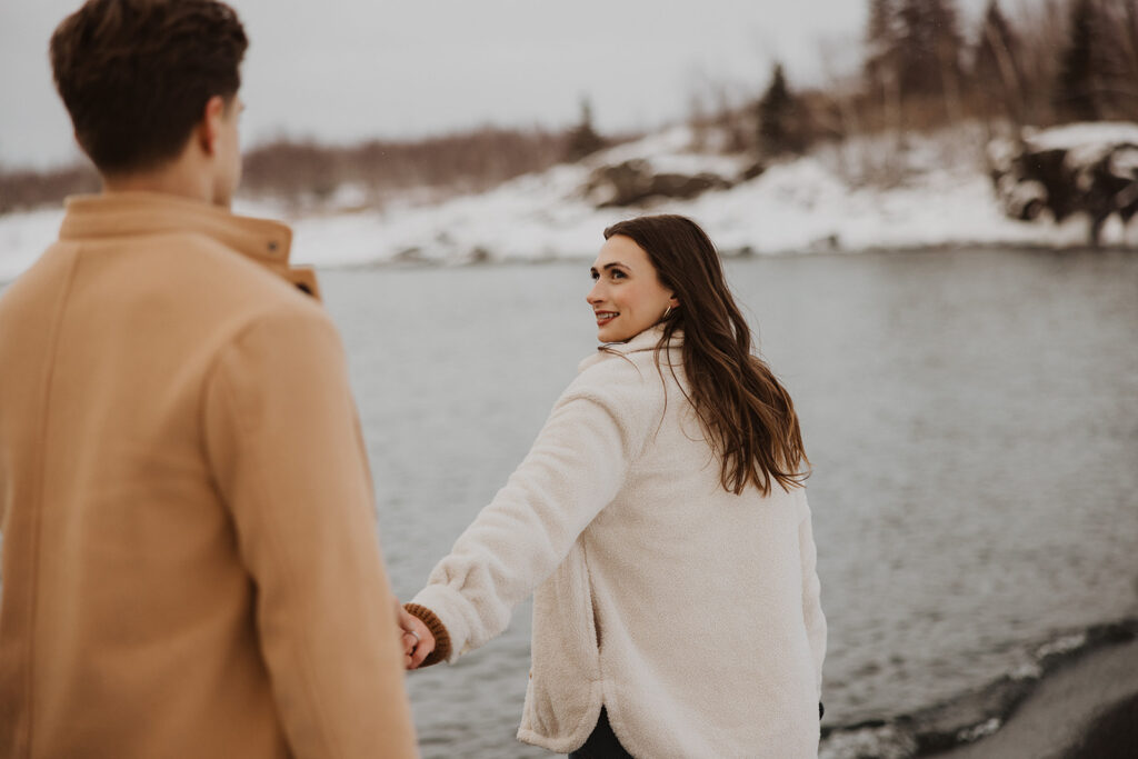 Woman looks back at her fiance as they walk along the shoreline on Black Beach in Minnesota