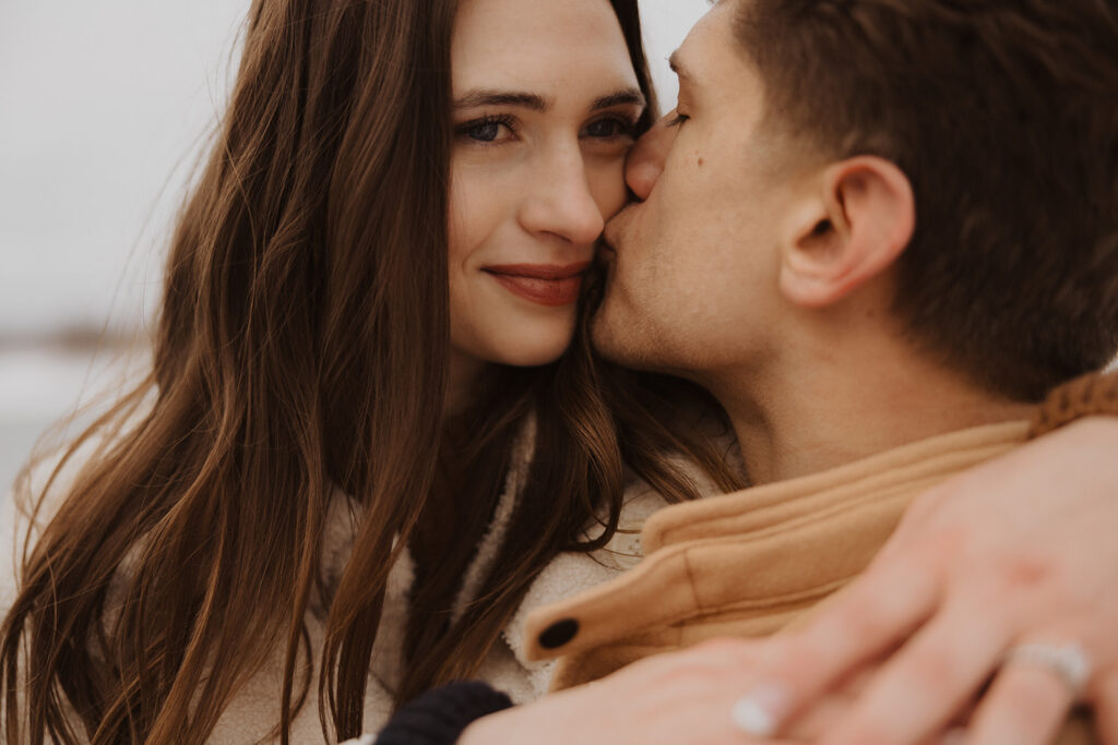 Man kisses woman's cheek during Black Beach destination engagement session in Minnesota