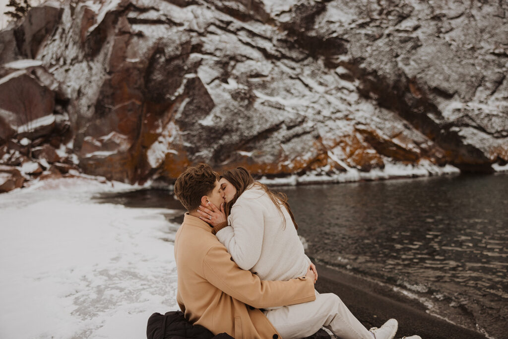 Engaged couple sits on Black Beach kissing near the water