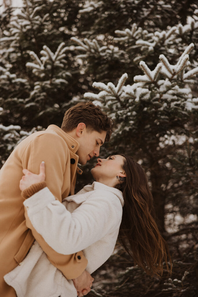 Man dips woman in a gentle kiss in front of the snow-kissed pines