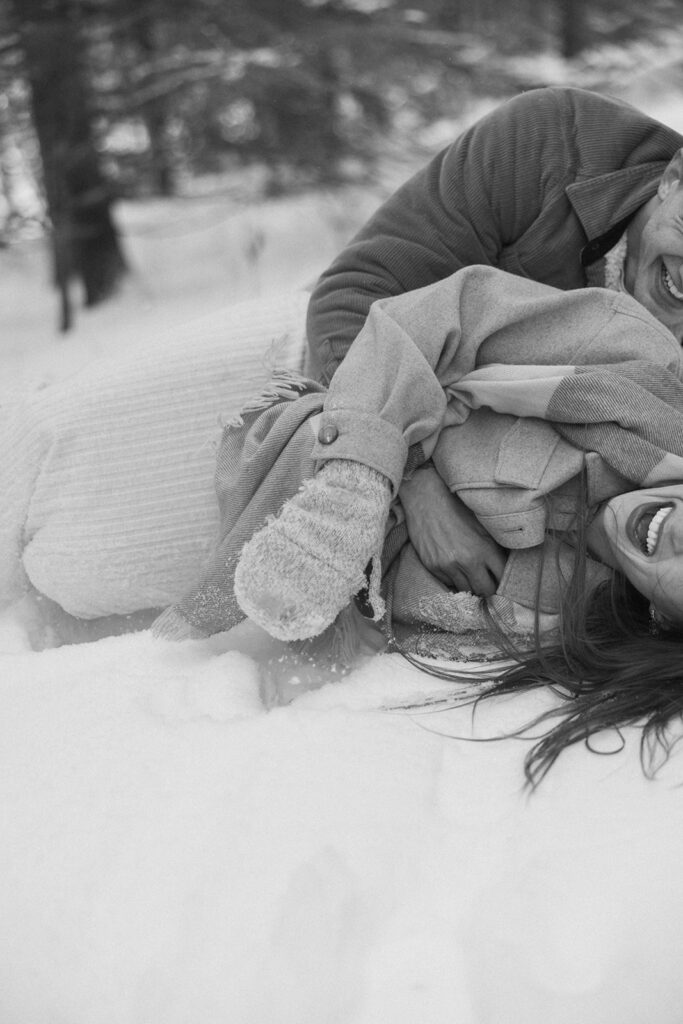 Engaged couple wrestles in the snow during Black Beach engagement photoshoot