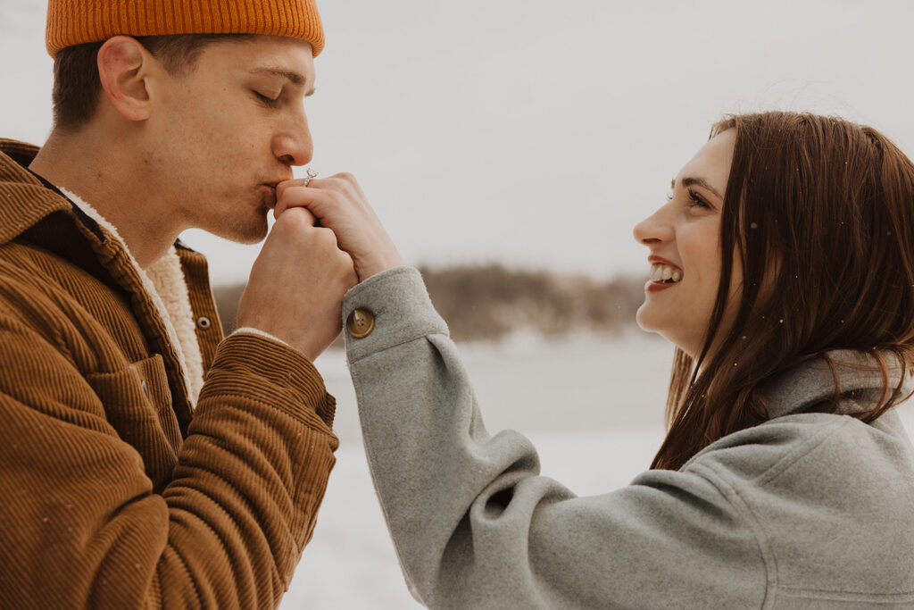 Man kisses woman's ring finger during Black Beach engagement session