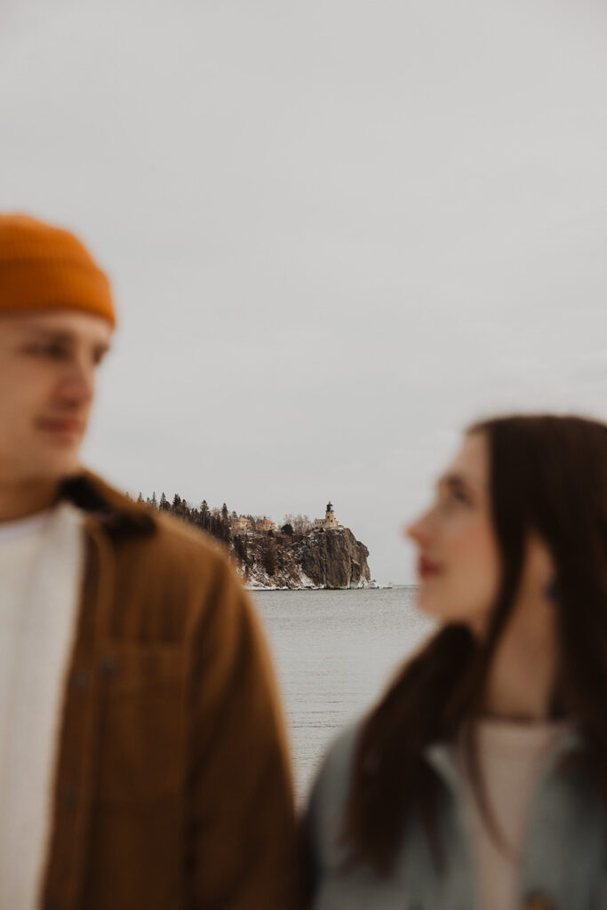 Man and woman look at each other as lighthouse on Silver Bay rises in the distance