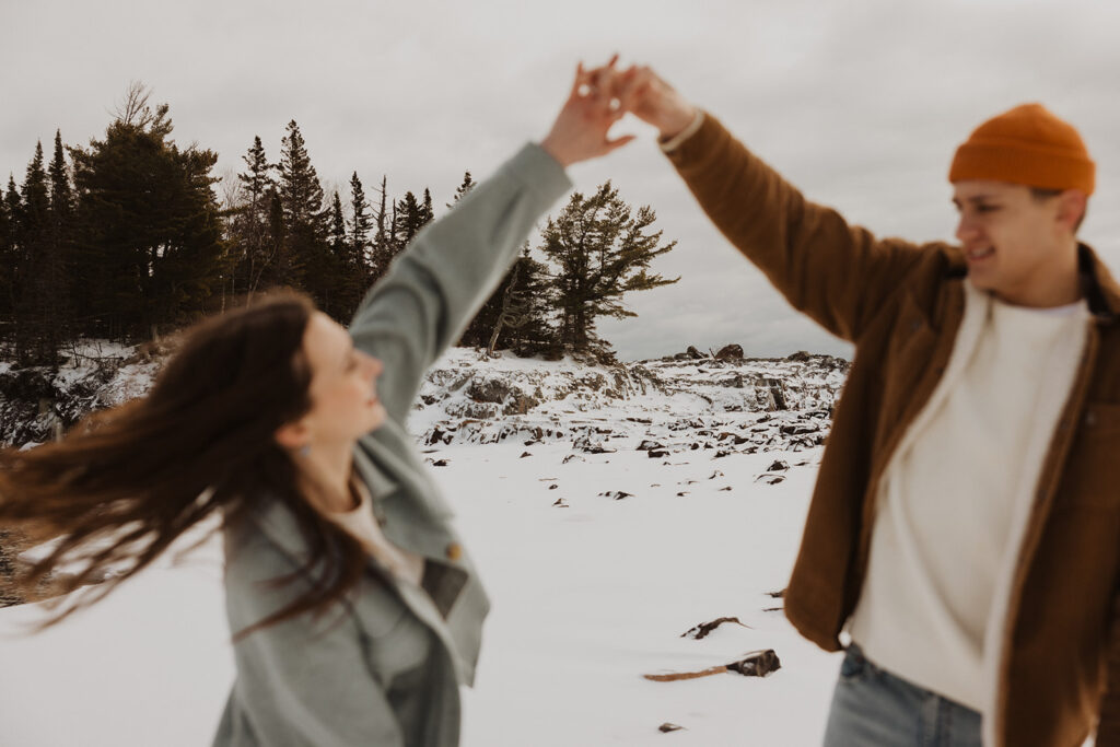 Man twirls woman around in the snow during winter engagement session on Black Beach in Minnesota