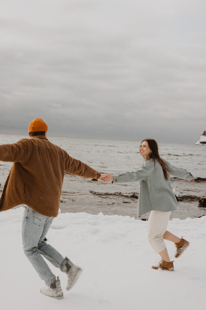 Engaged couple in love dances and holds hands in the snow on Black Beach of North Shore