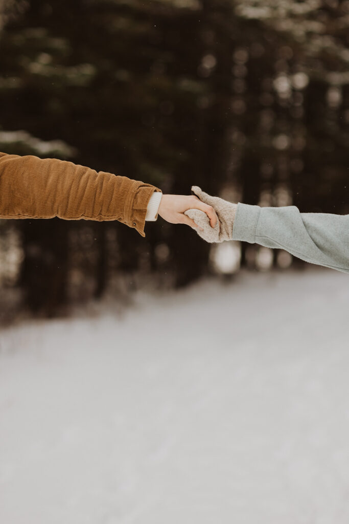 Engaged couple holds mittened hands during Black Beach in Silver Bay engagement