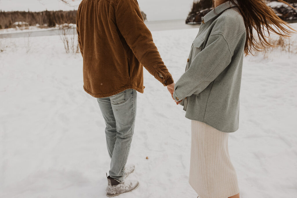 Engaged couple holds hands during snowy Black Beach engagement