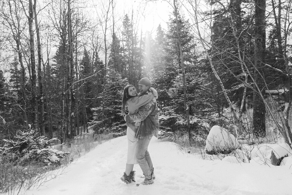 Engaged couple twirls in the cascading sunlight in North Shore snowy forest