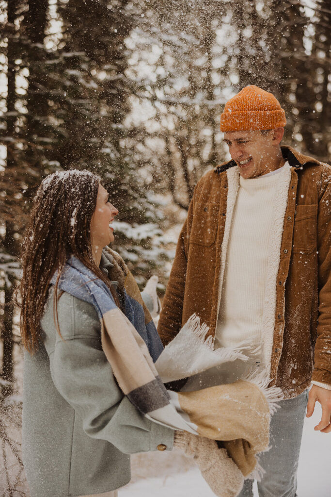 Woman throws snow on man during Black Beach destination engagement photoshoot