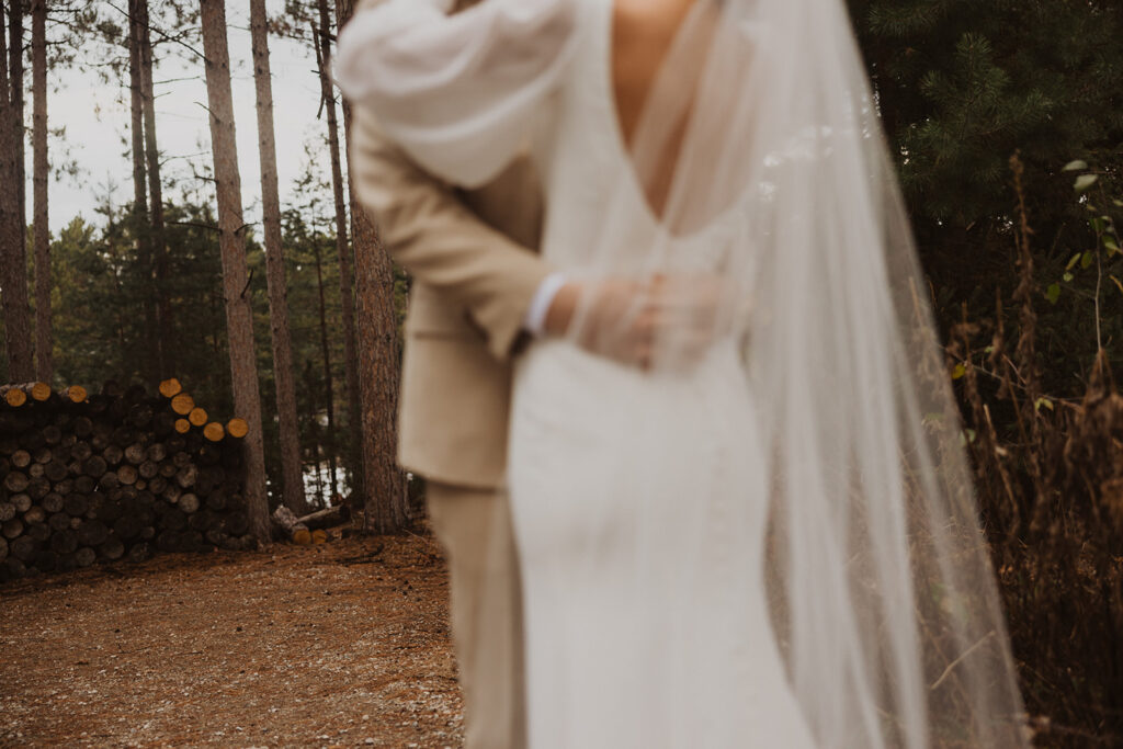 Bride and groom embrace under pines at winter wedding venue in Minnesota