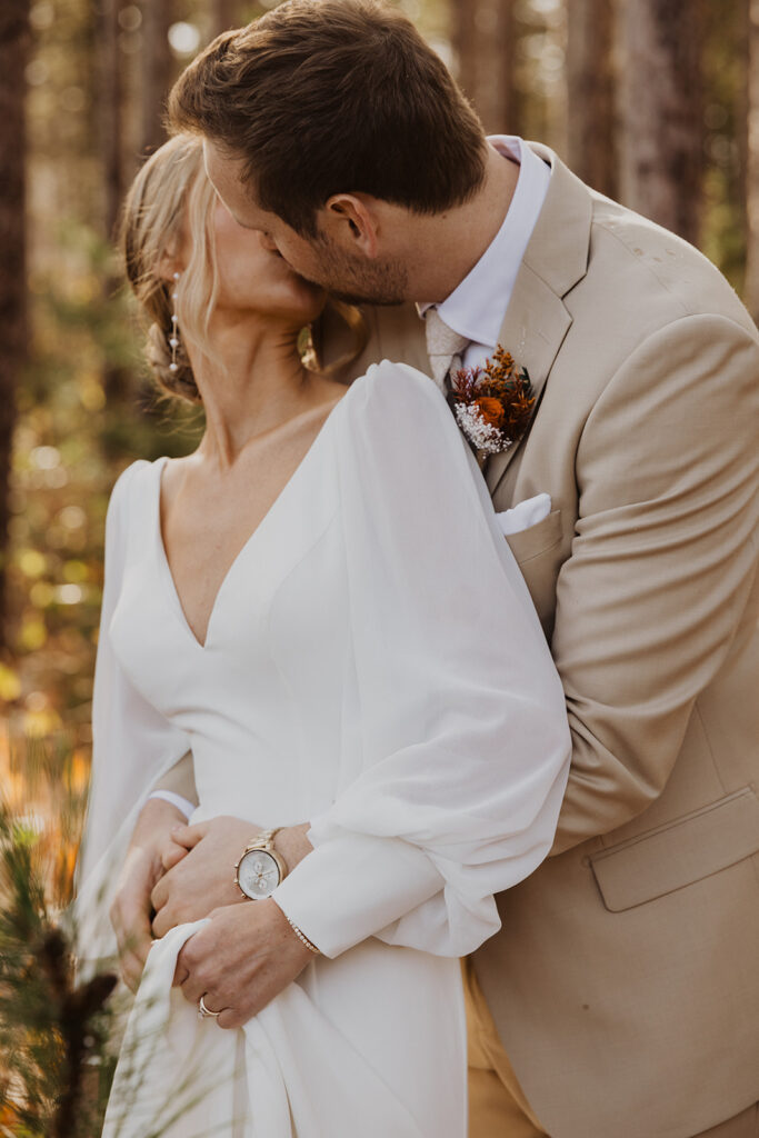 Groom kisses bride tenderly under the cover of the pines at winter wedding venue in Minnesota