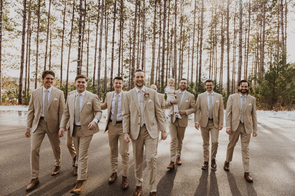 Groom and groomsmen and ring bearer smile at winter wedding venue 