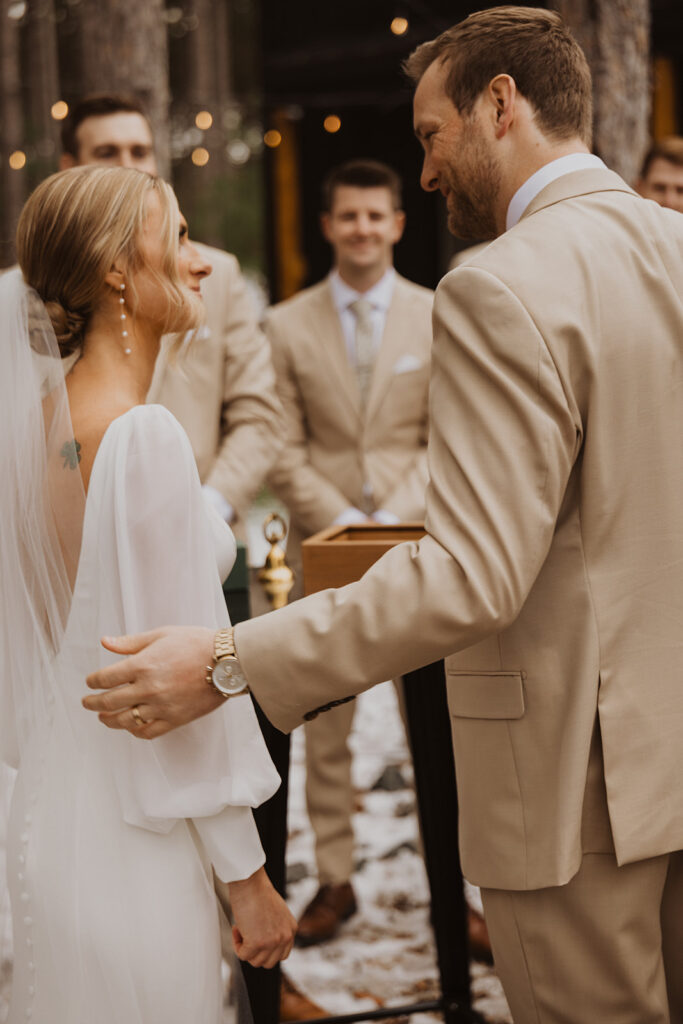 Groom puts his hand on small of bride's back during their winter wedding ceremony