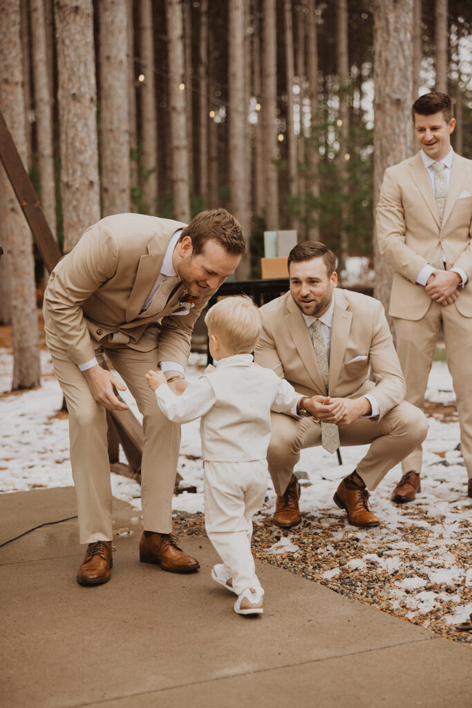 Groom bends down to greet toddler ring bearer as he reaches the end of the aisle