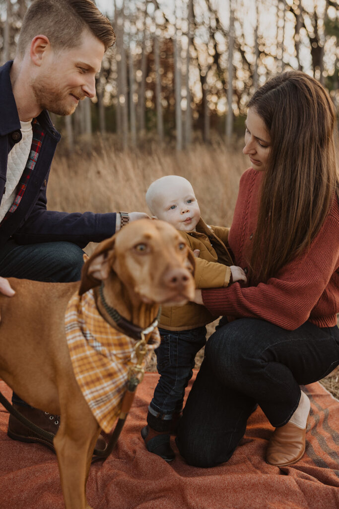 Young family with dog sits on comfy red blanket during autumn mini photography session