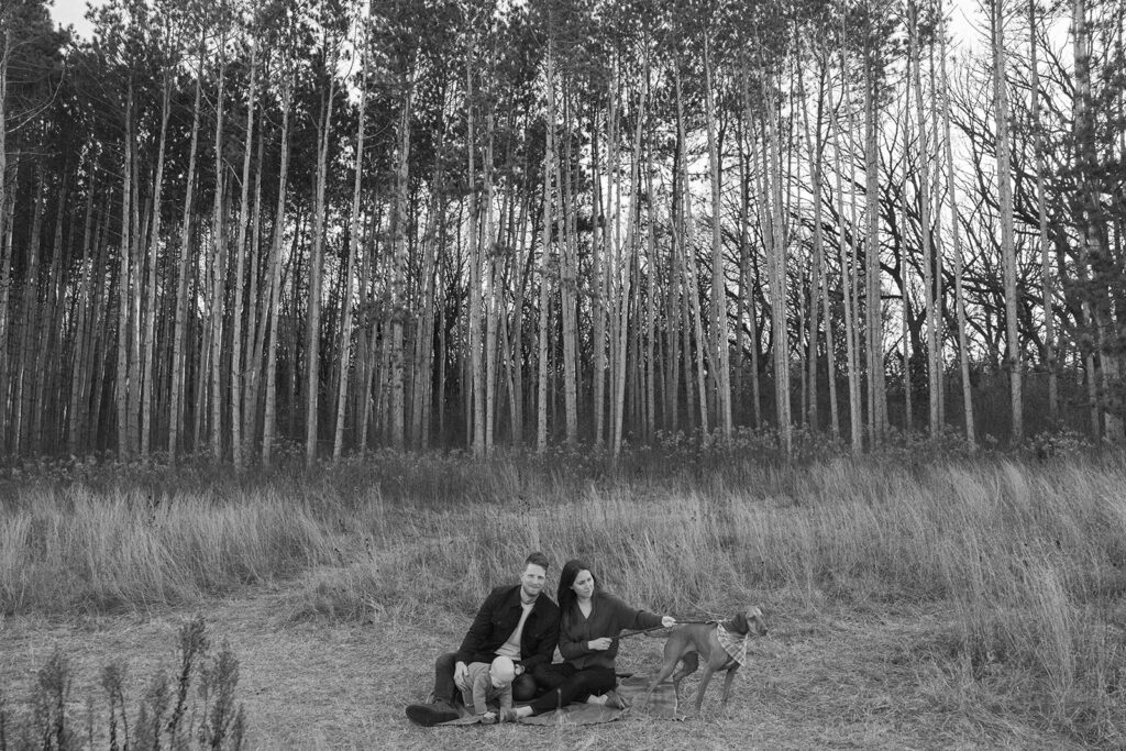 Parents, baby, and dog sit in an open Minnesota field during family photography with dogs