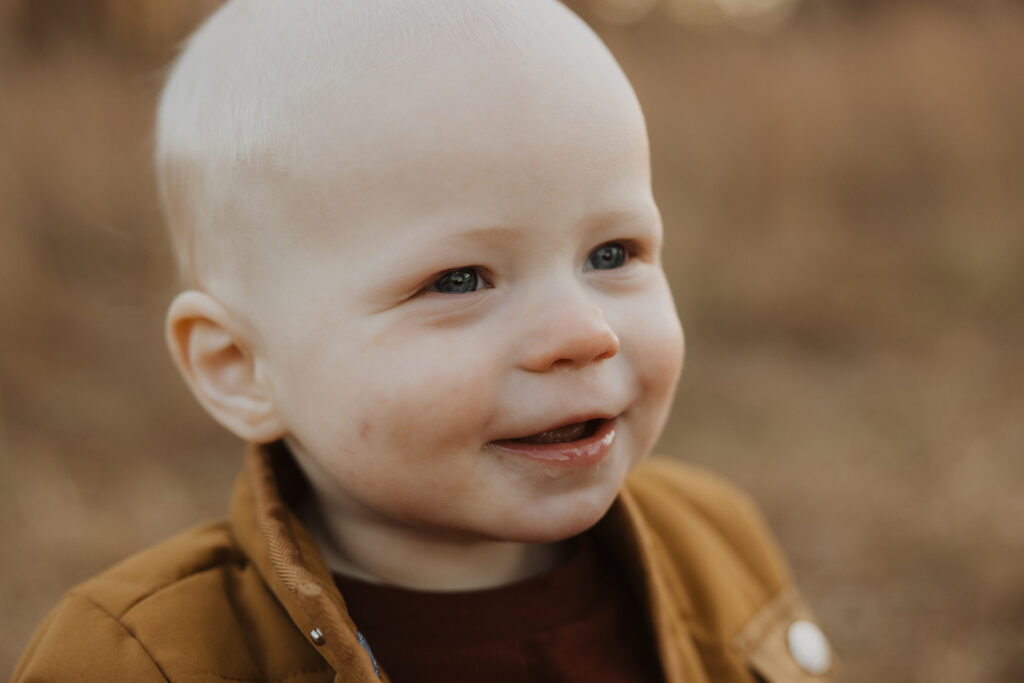 Baby gives cheesy smile in autumn family photography with dogs session