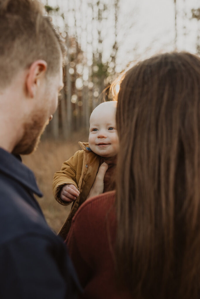 Baby beams up at his parents as they hold him in the air