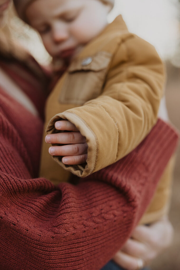 Baby boy plays with his Carharrt coat sleeve during family photography with dogs