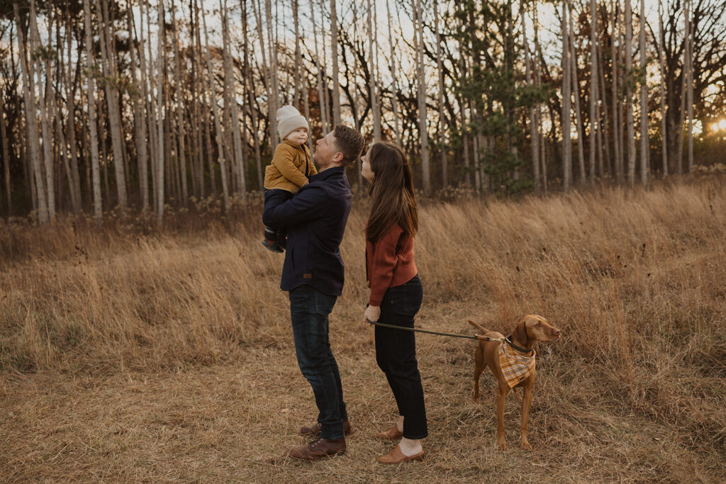 Parents play with their young son as they hold onto their dog in Minnesota field