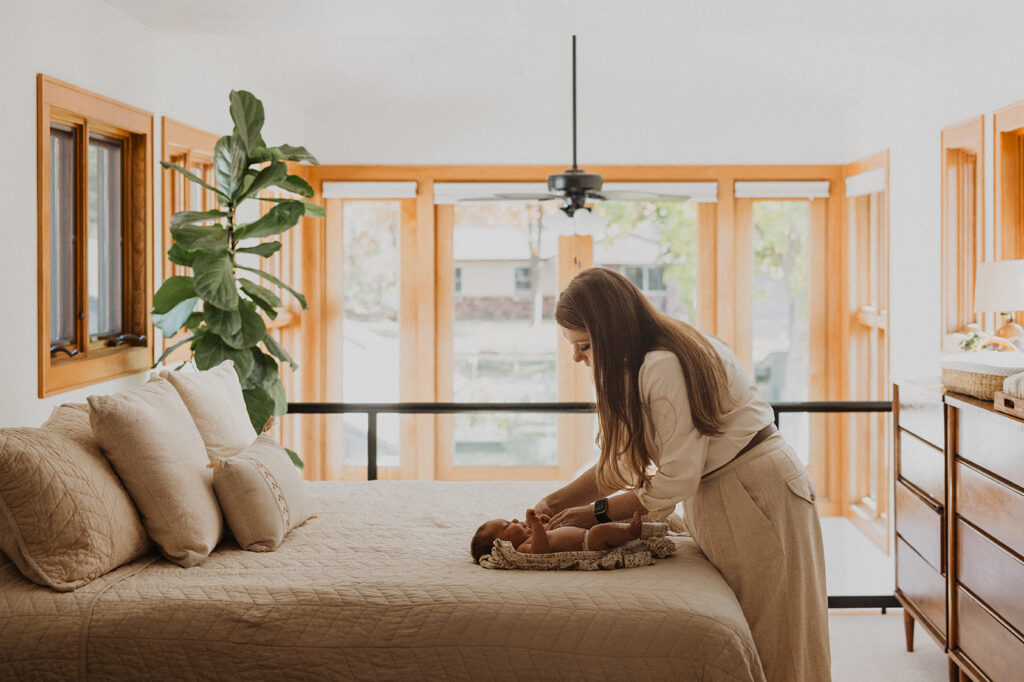 Mom changes newborn baby's diaper on beige-quilted bed