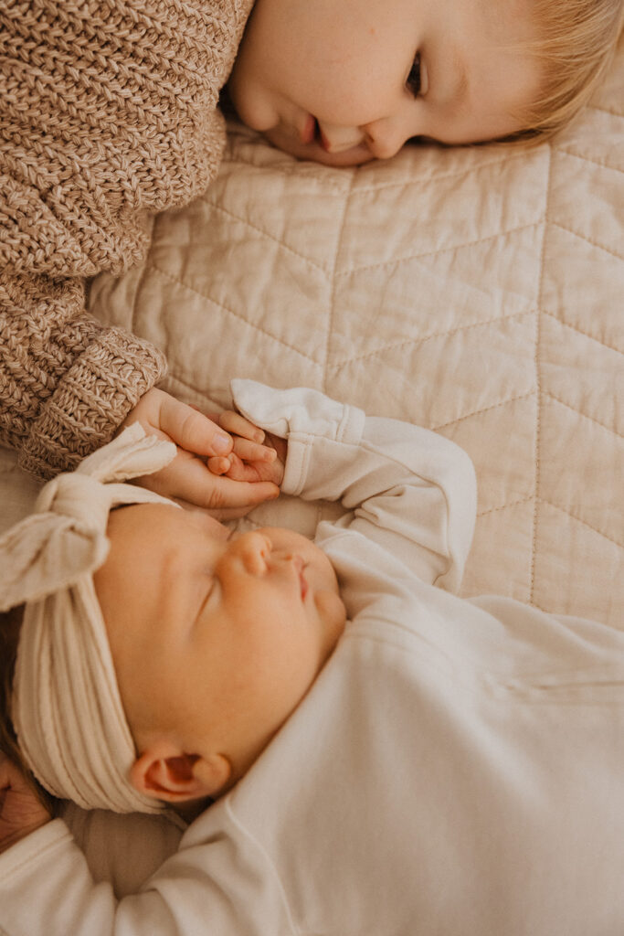 Young boy plays curiously with newborn baby sister's hands