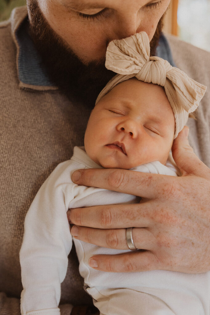 Dad kisses newborn baby's bow-clad head