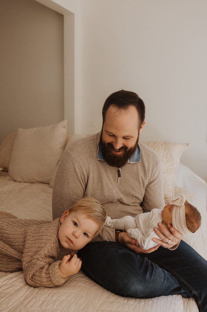 Young boy rests his head on his dad's knee during newborn photography with family