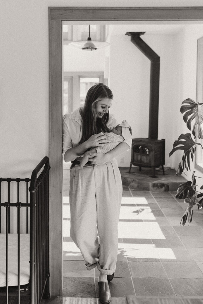 Mom leans against door frame while holding newborn baby in newborn photography with family