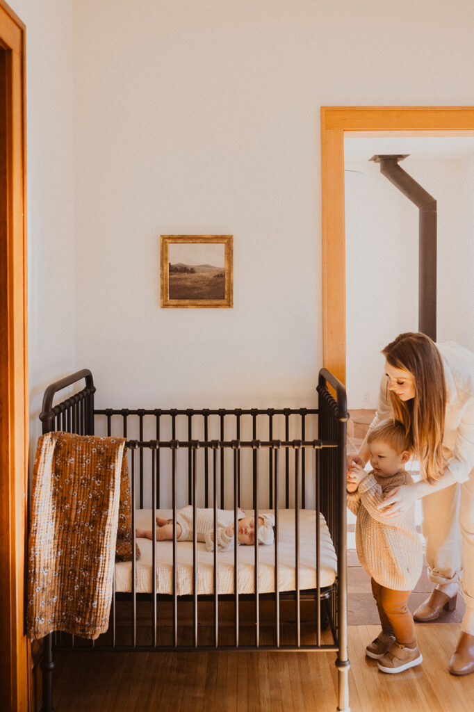 Mom and little boy look through crib bars at newborn baby in Minnesota newborn photography with family