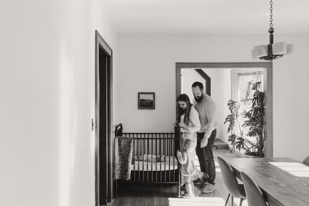 Young family peeks in crib at newborn baby in newborn photography with family in Minnesota