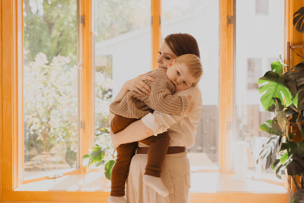 Toddler cuddles his mom in Nordic kitchen spilling with natural light