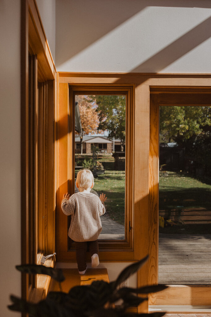 Little boy looks out the window of his new home in newborn photography with family