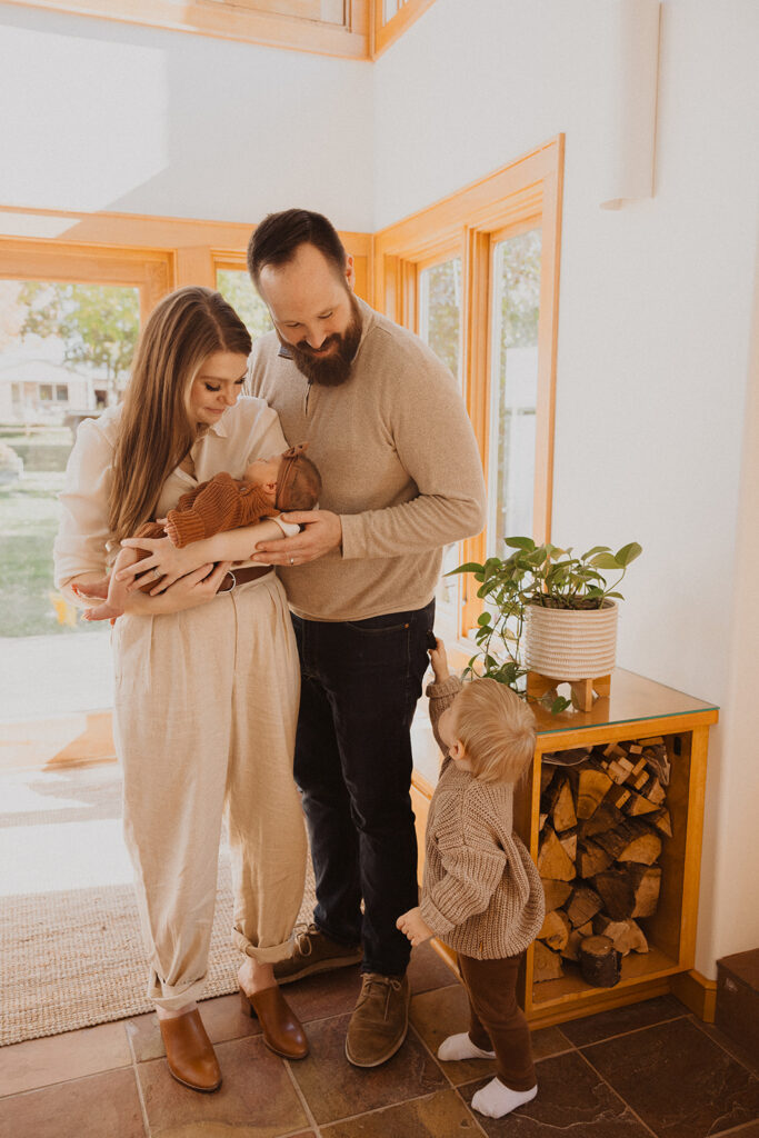 Little boy reaches for his dad as he and his wife look down at their newborn child