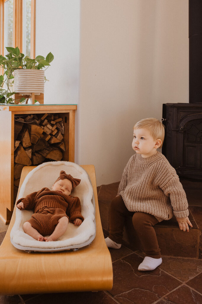 Toddler in knit sweater sits next to newborn in knit set in Nordic newborn photography with family in Minnesota