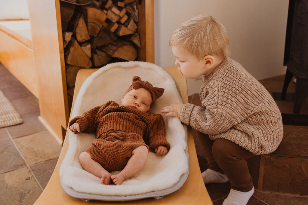 Toddler boy curiously peeks at his newborn baby sister