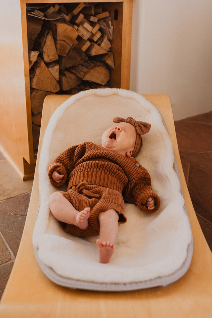 Newborn baby wearing cozy knit set yawns as she lays in front of wood stack